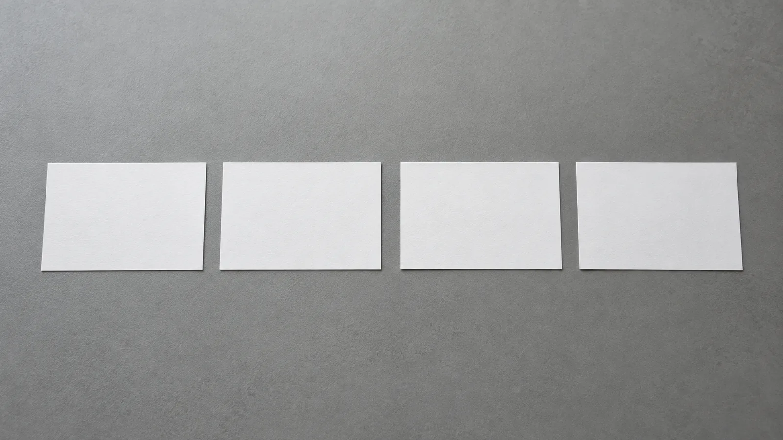 Four blank white cards laid out in an evenly spaced row on a flat grey surface.